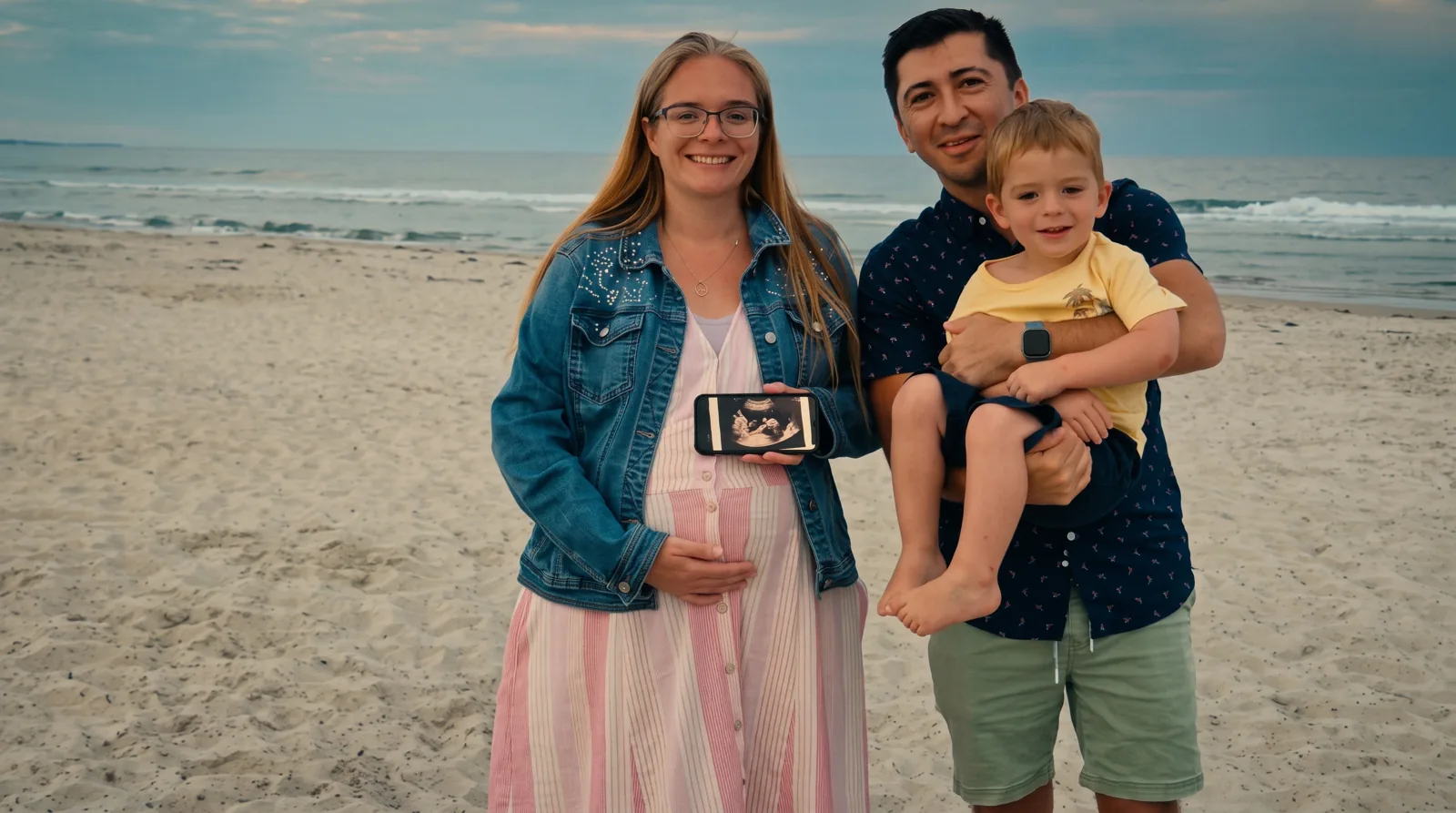 The EternalGrace Hub family standing together on a beach at dusk, holding an ultrasound photo.